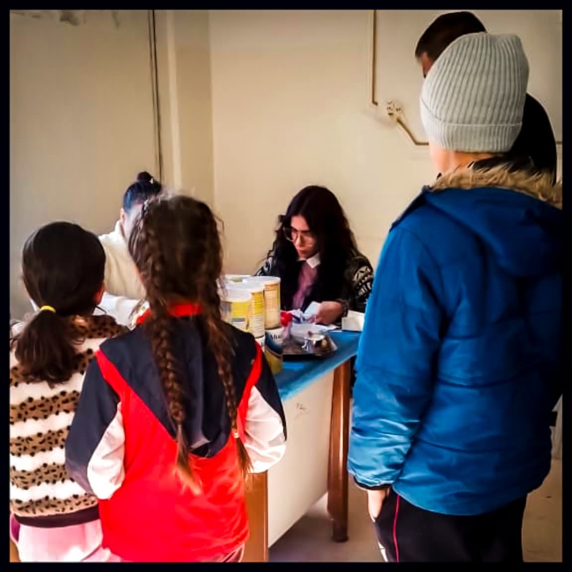 Children waiting at a counter as a health worker prepares nutritional supplies